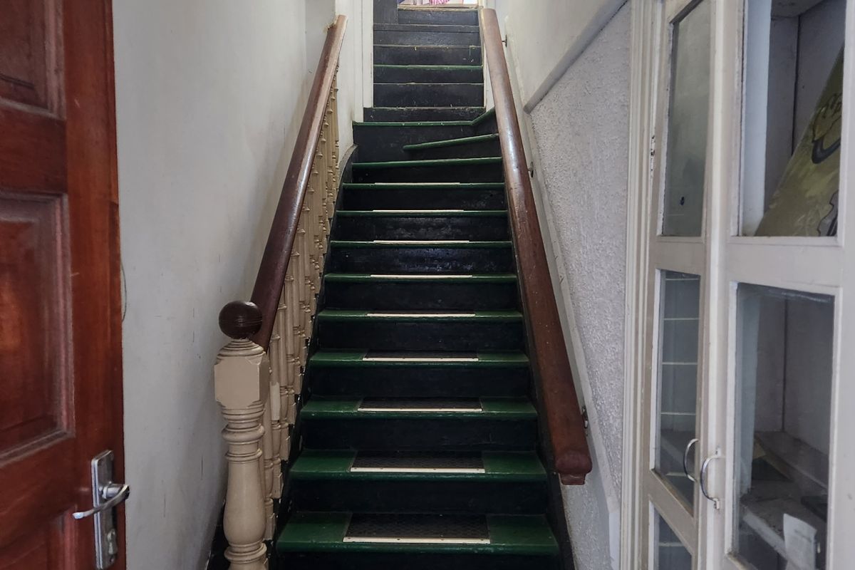 A narrow interior hallway featuring a traditional timber staircase with a decorative balustrade and an adjacent built-in glass display cabinet.