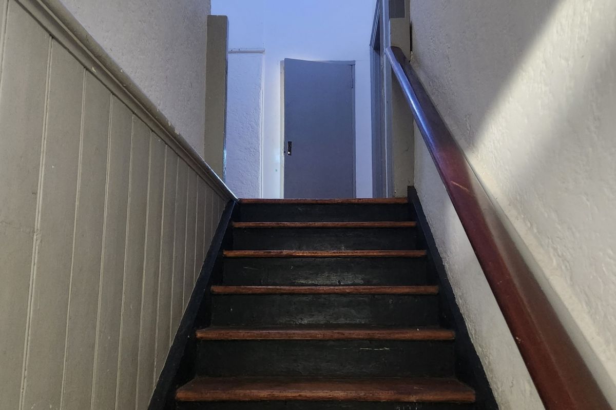 A narrow interior staircase featuring timber treads, a wooden handrail, and traditional wainscoting leading to an upper landing.