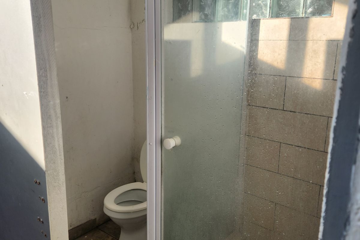 A functional bathroom featuring a toilet and a separate shower enclosure with glass block detailing and tiled finishes.
