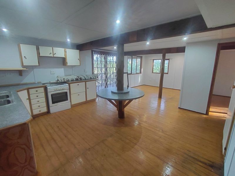 Spacious open-plan kitchen and living area featuring timber flooring, exposed beams, recessed lighting, and functional built-in cabinetry with a central breakfast counter.