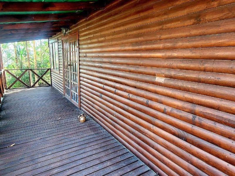 A covered timber balcony featuring log-style wall cladding, wooden decking, and a timber balustrade, providing an outdoor space with direct access to the interior.