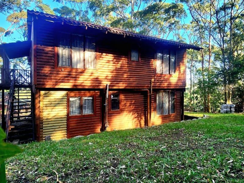 A two-story log cabin style townhouse exterior featuring timber cladding, a raised balcony with staircase, and surrounding garden area.