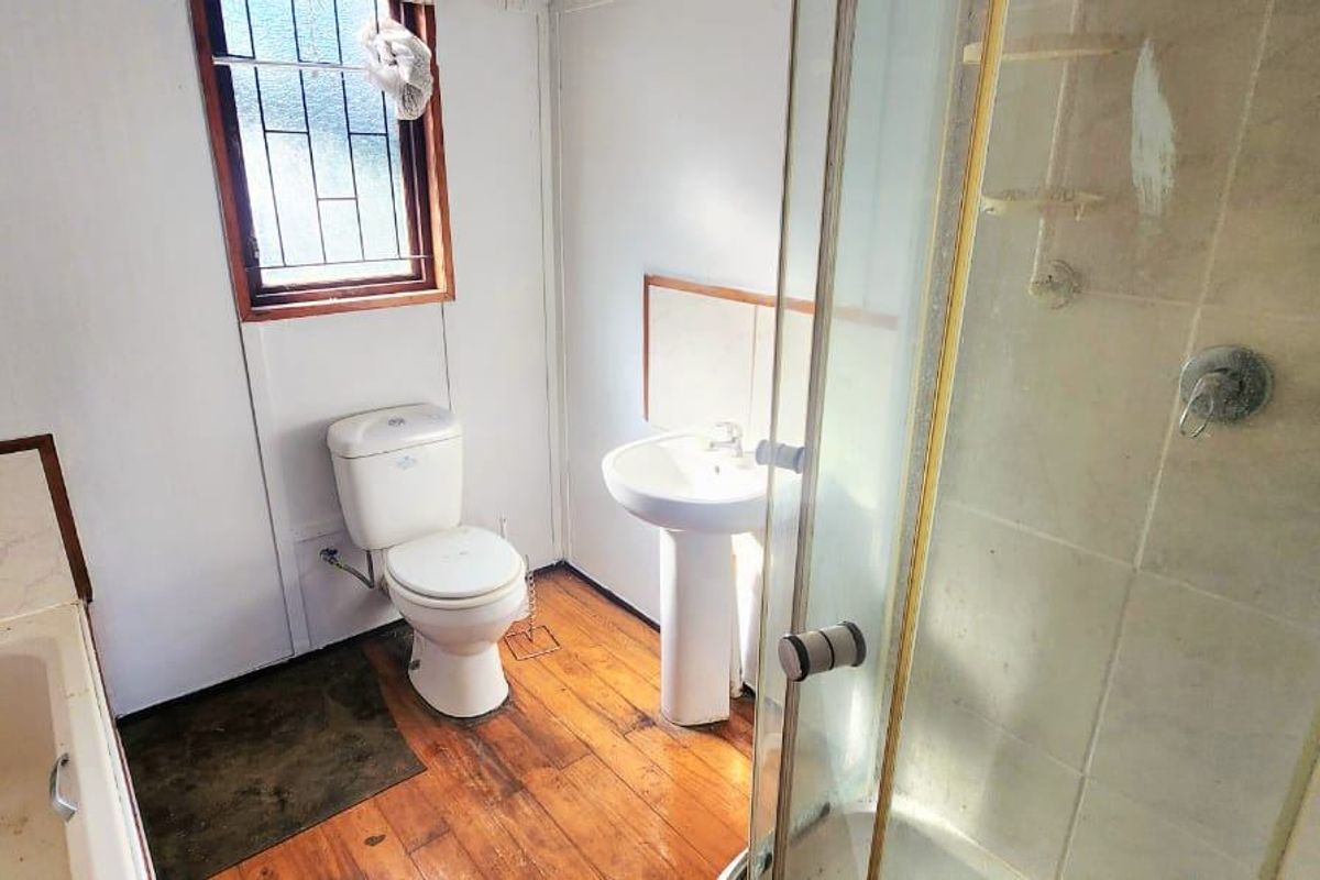 A functional bathroom featuring a pedestal basin, toilet, bathtub, and separate shower enclosure with timber flooring and security bars on the window.
