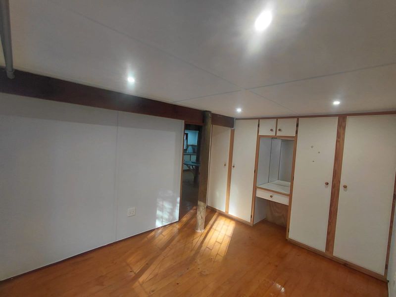 A bedroom featuring built-in cupboards with an integrated vanity station, recessed lighting, and timber flooring.