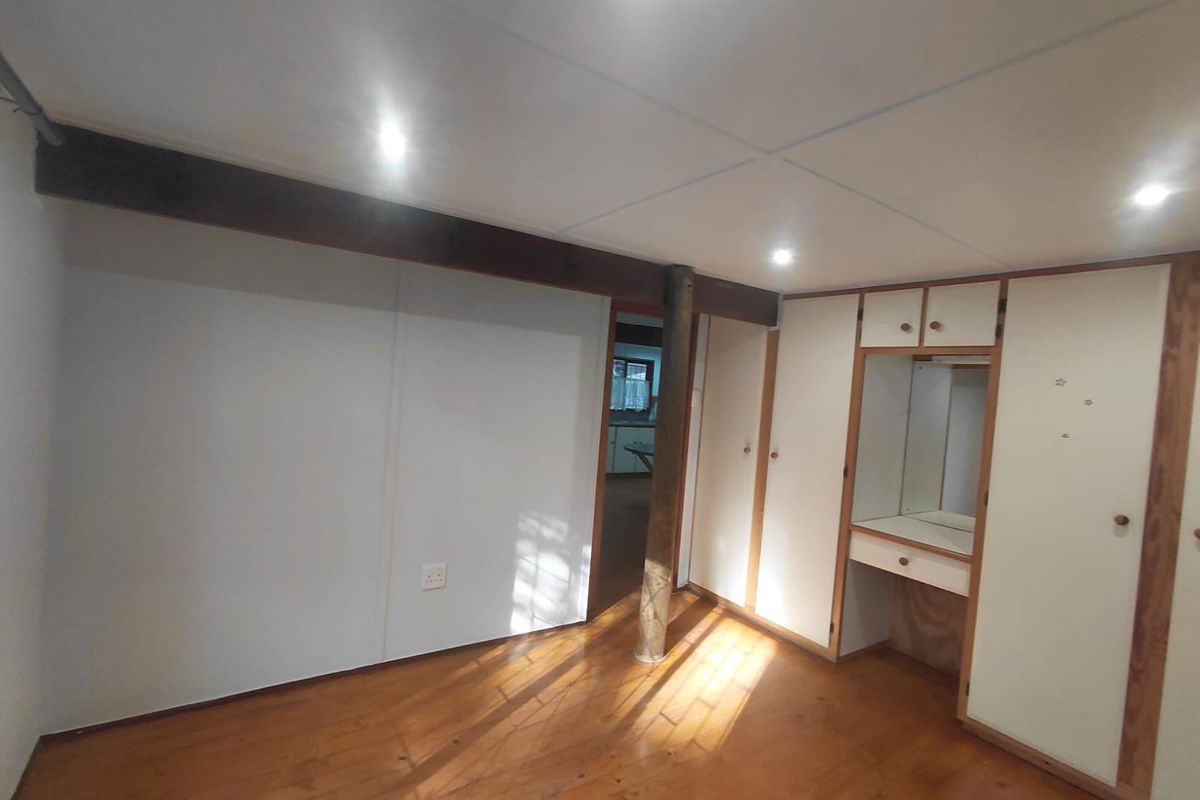A spacious bedroom featuring timber flooring, recessed lighting, and extensive built-in cabinetry with an integrated vanity area.
