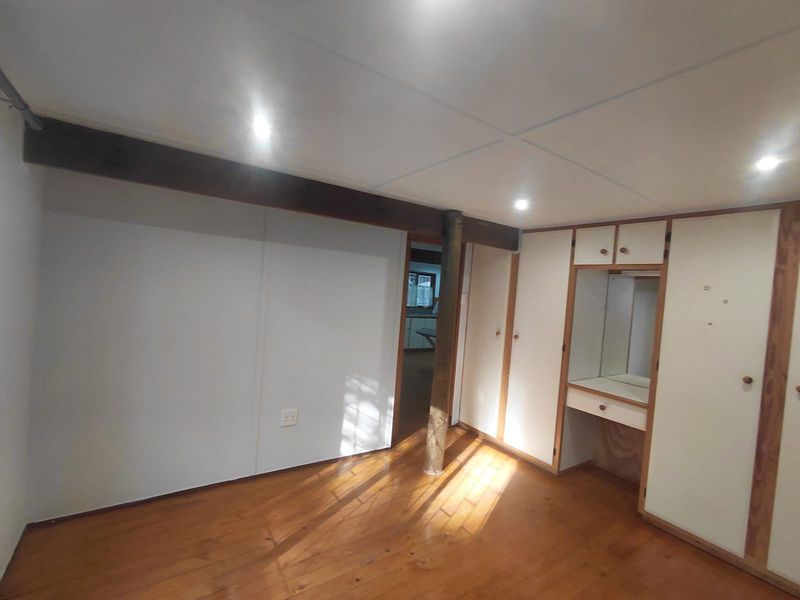 A spacious bedroom featuring timber flooring, recessed lighting, and extensive built-in cabinetry with an integrated vanity area.