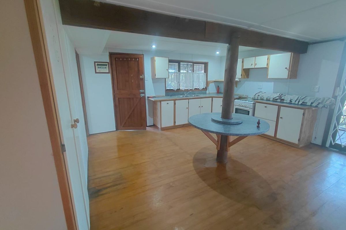 A dated kitchen featuring timber flooring, exposed structural beams, and built-in cabinetry with a central breakfast bar island.