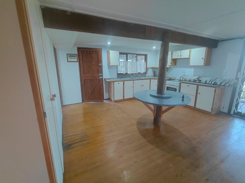 A dated kitchen featuring timber flooring, exposed structural beams, and built-in cabinetry with a central breakfast bar island.