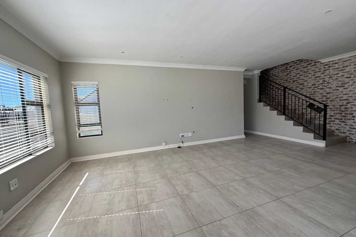 Spacious, empty living area featuring large format floor tiles, a decorative exposed brick wall, and a staircase with a wrought iron balustrade.