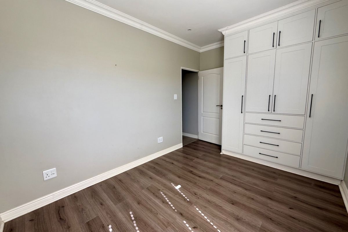 A bright, empty bedroom featuring modern laminate flooring, crown molding, and extensive built-in cabinetry with clean, contemporary finishes.