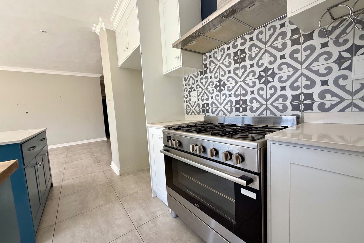 Modern kitchen featuring a stainless steel gas stove, extractor fan, patterned tile backsplash, and ample built-in cabinetry with stone countertops.