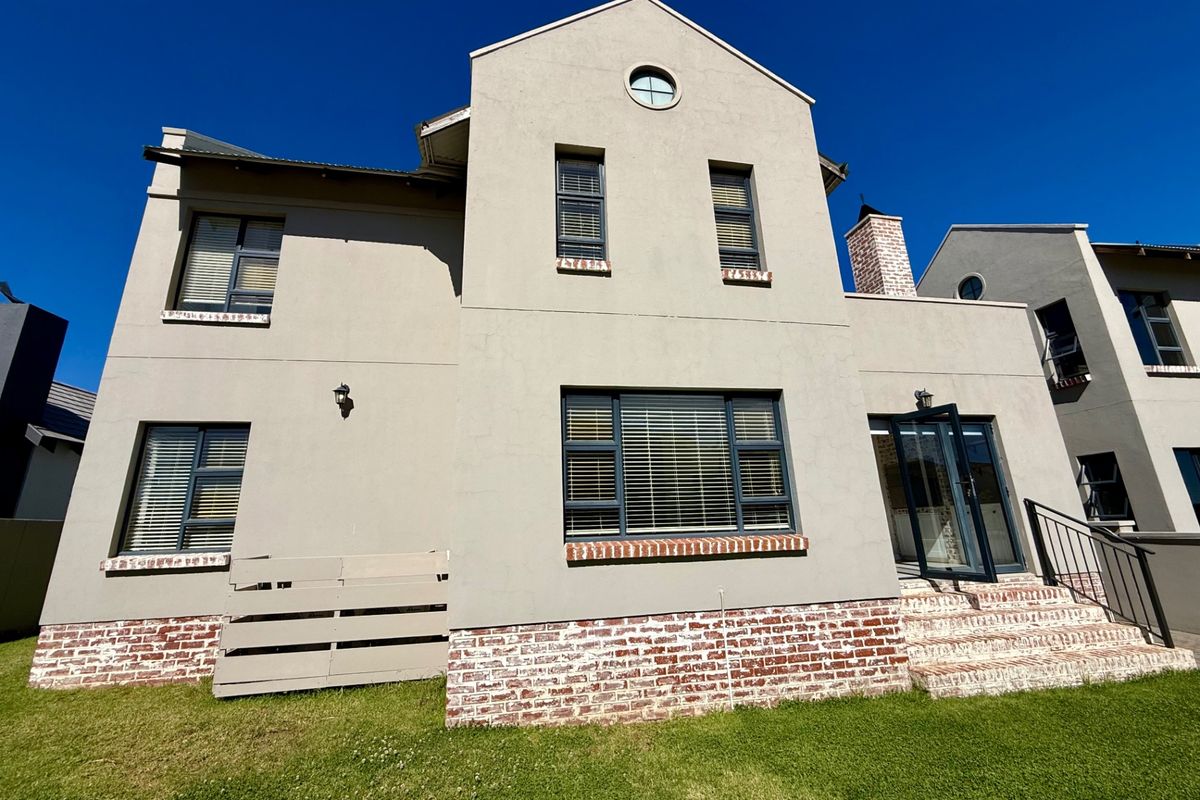 Rear elevation of a two-story townhouse featuring plastered walls, brick detailing, aluminium window frames, and a small brick staircase leading to the garden.