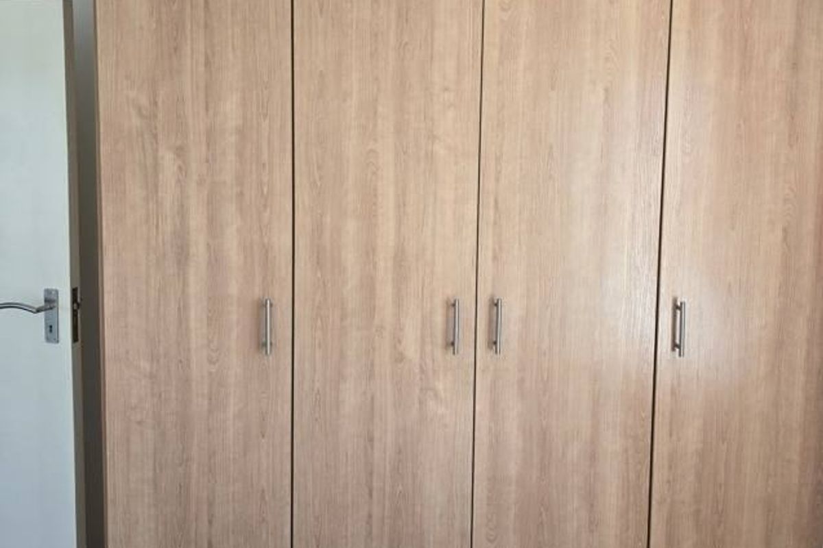 A bedroom featuring a large, light wood-grain built-in wardrobe with modern metal handles.