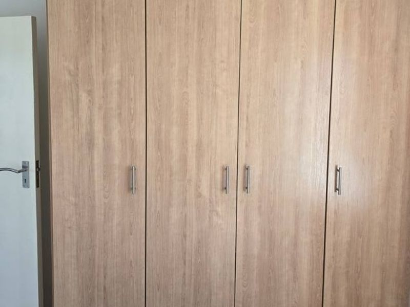 A bedroom featuring a large, light wood-grain built-in wardrobe with modern metal handles.