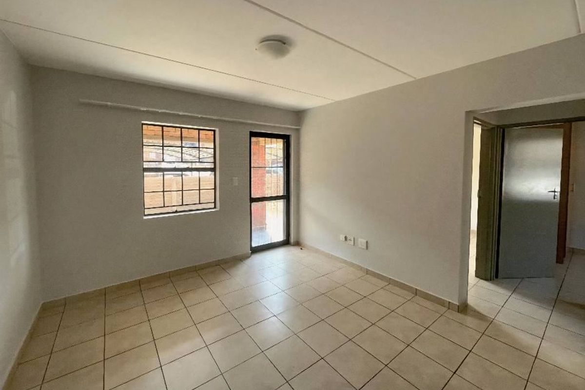 A bright, empty living room featuring neutral tiled flooring, a security-fitted window, and direct access to an outdoor area.