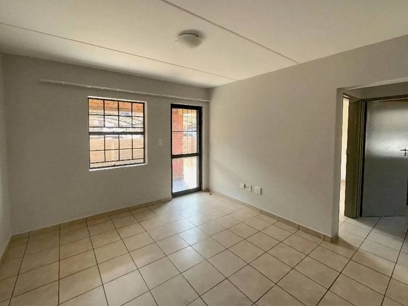 A bright, empty living room featuring neutral tiled flooring, a security-fitted window, and direct access to an outdoor area.