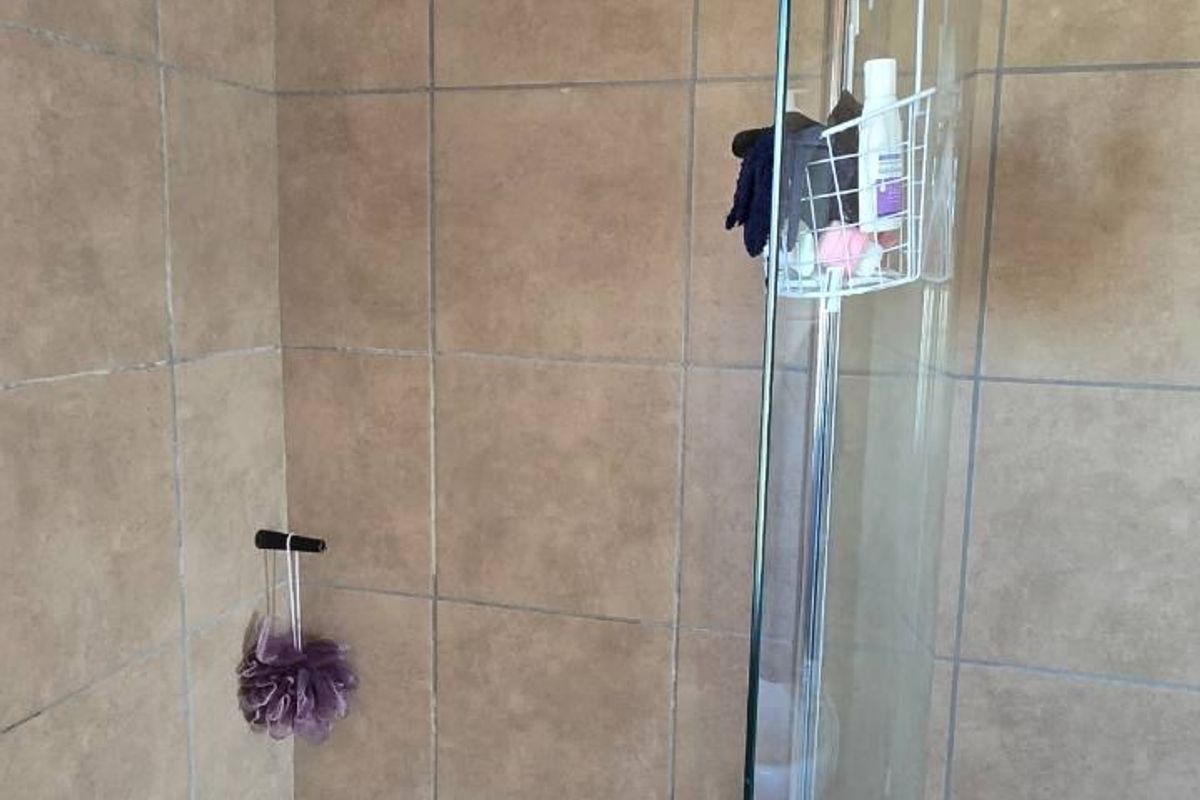 A shower enclosure featuring tiled walls, a glass screen, and a standard shower head, showing signs of wear in the grout lines.