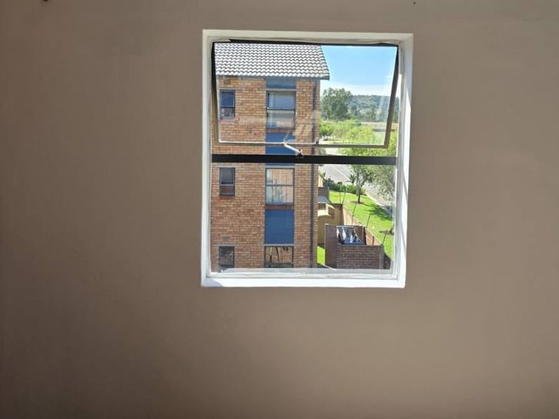 An empty bedroom featuring a top-hung window with an exterior view and a built-in cupboard.