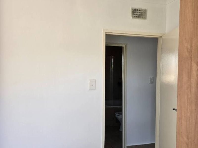A simple hallway area with tiled flooring, leading into an adjacent bathroom space.