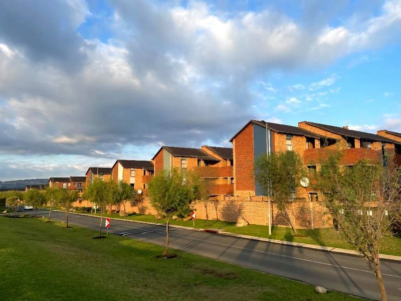 A street-level view of a residential apartment complex featuring multi-story brick buildings with pitched roofs and surrounding landscaped grounds.