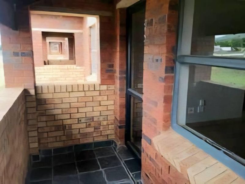 A covered balcony area featuring exposed brick walls and tiled flooring, providing an outdoor transition space with access to the interior.