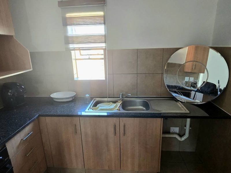 A functional kitchen area featuring laminate cabinetry, granite countertops, a stainless steel sink, and tiled splashbacks with a window for natural light.