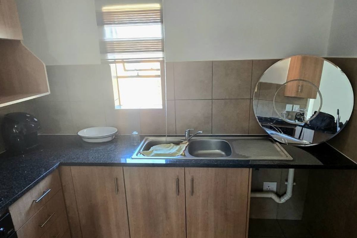 A functional kitchen area featuring laminate cabinetry, granite countertops, a stainless steel sink, and tiled splashbacks with a window for natural light.