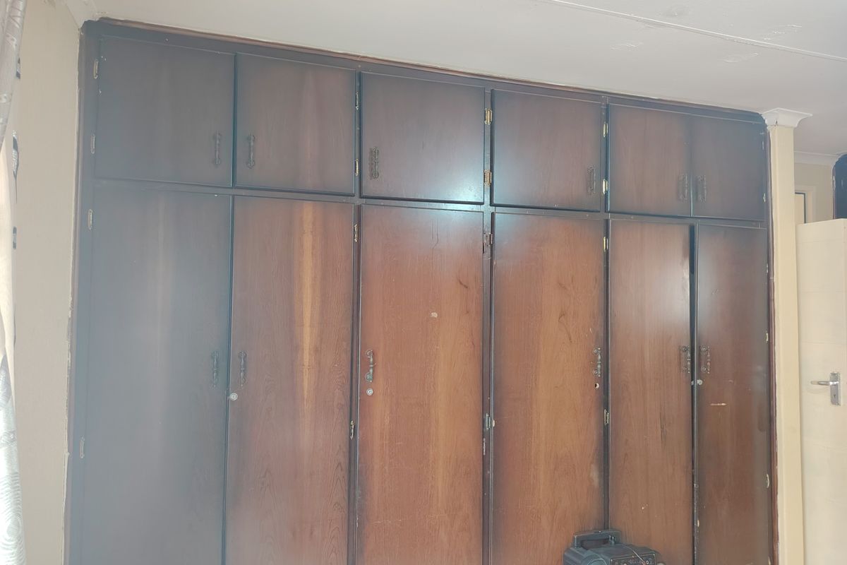 A bedroom featuring extensive floor-to-ceiling built-in wooden cupboards, providing ample storage space with a dated aesthetic.