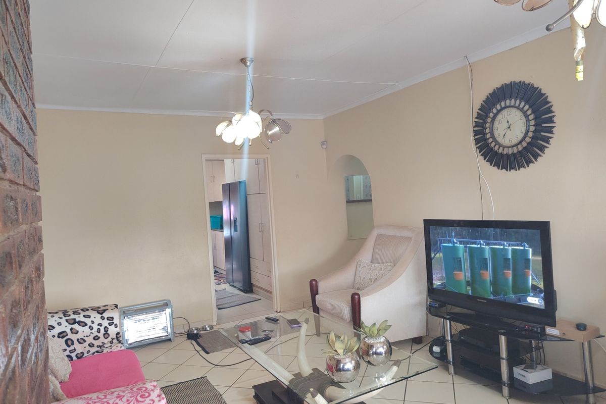 A living room featuring tiled flooring, an exposed brick pillar, and an arched doorway leading to the kitchen area.