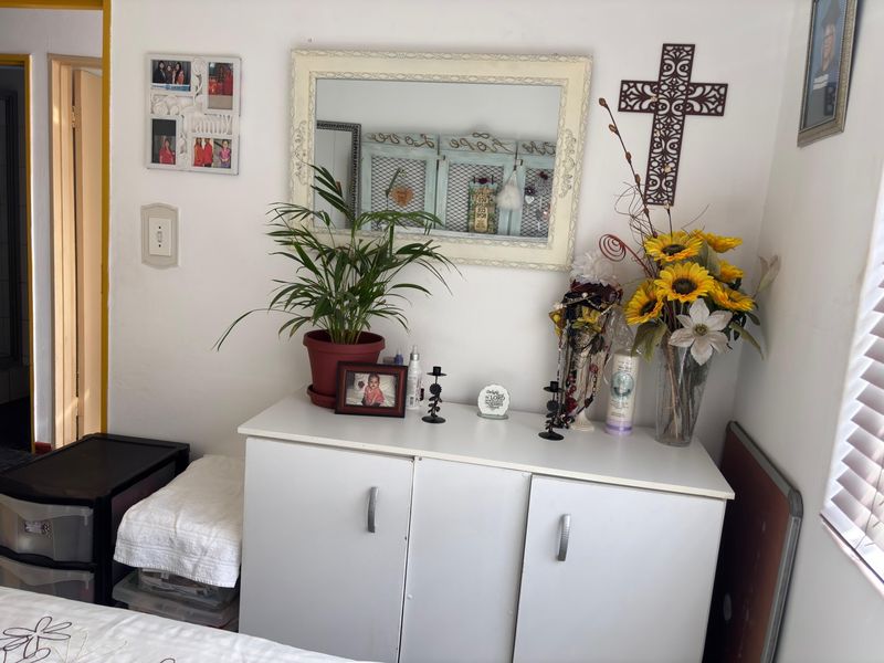 A bedroom interior featuring a white storage cabinet, wall-mounted mirror, and window with blinds.
