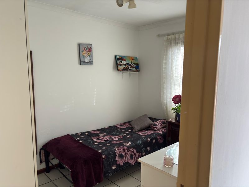 A compact bedroom featuring tiled flooring and a built-in cupboard, offering a functional space with natural light.