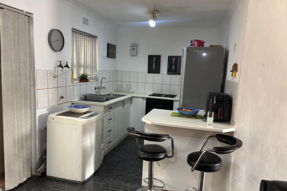 A compact kitchen featuring built-in cabinetry, a tiled backsplash, a breakfast counter, and integrated cooking appliances, requiring cosmetic updates to modernize the space.