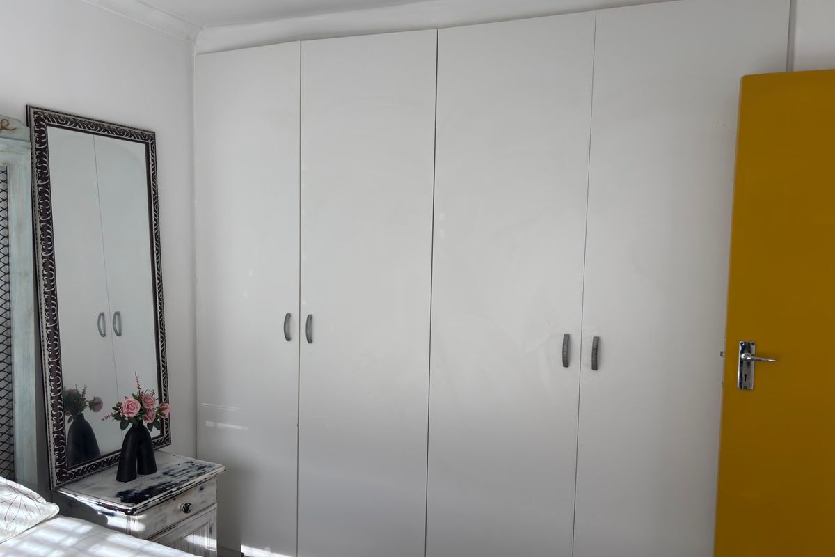 A bedroom featuring a large, white built-in wardrobe with modern handles, providing ample storage space.