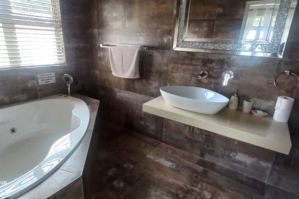 Modern bathroom featuring a corner spa bath, wall-mounted basin, and dark tiled finishes throughout.