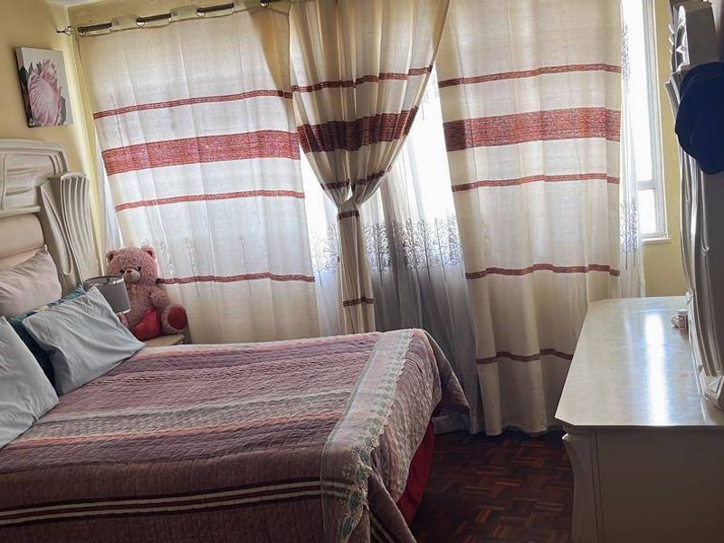 A bedroom featuring parquet flooring and large windows with curtains, providing natural light to the space.