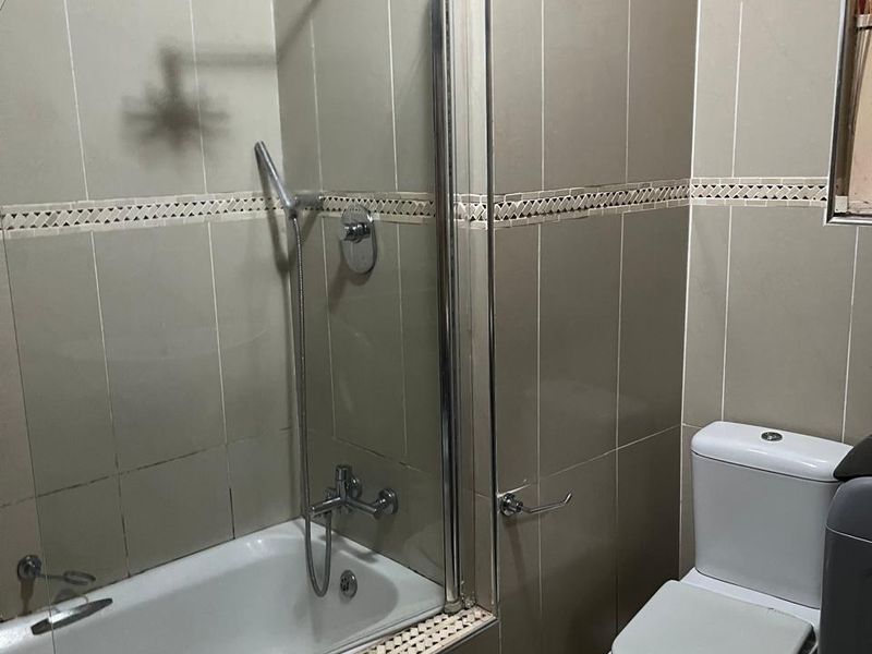 A functional bathroom featuring a bathtub with a glass shower screen, wall-mounted shower head, and a standard toilet.