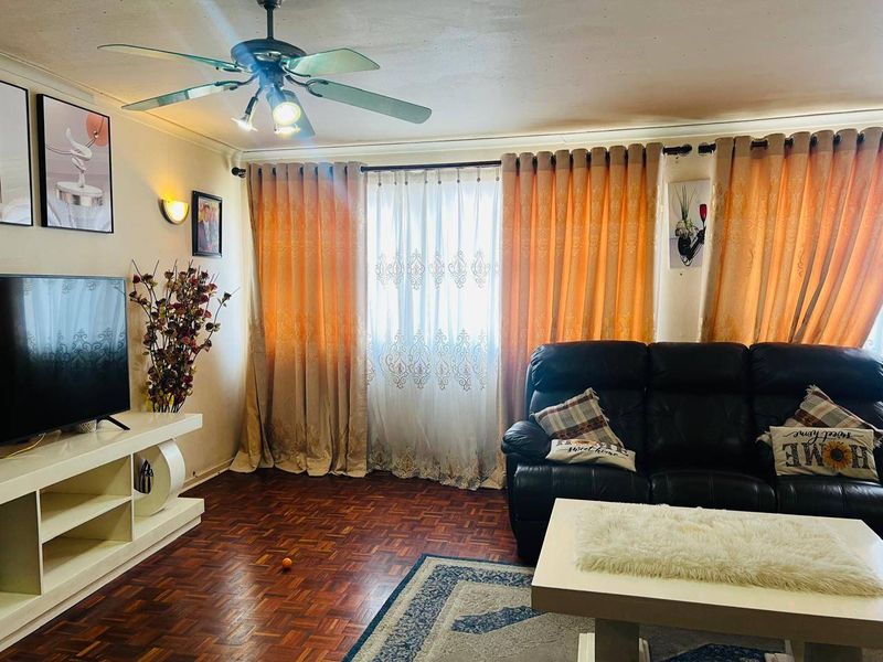 A living room featuring parquet flooring, a ceiling fan, and large windows dressed with floor-to-ceiling curtains.