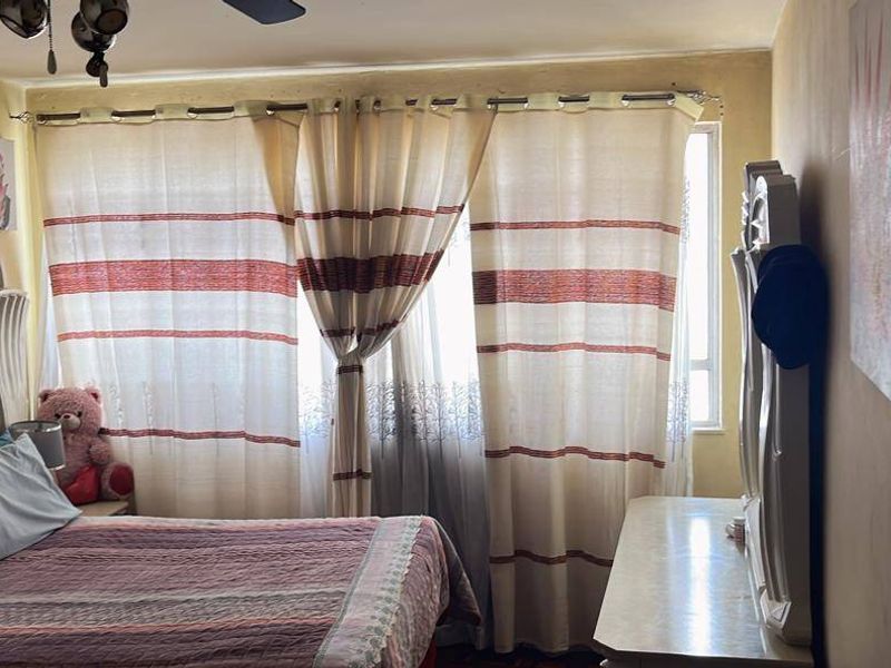 A bedroom featuring a window with curtains, a ceiling fan, and neutral wall tones, providing a functional and comfortable sleeping space.