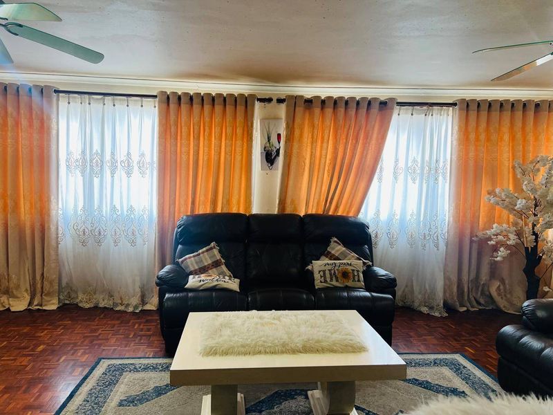 A living room featuring parquet flooring, dual ceiling fans, and large windows dressed with layered curtains.