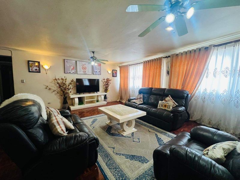 A spacious living room featuring parquet flooring, ceiling fans, and large windows with curtains, providing a comfortable and functional living area.