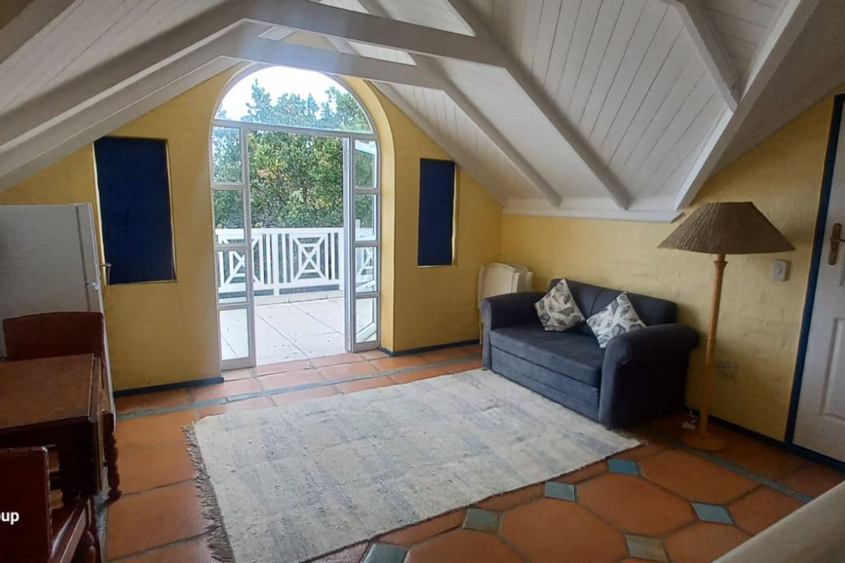 Spacious attic-style living room featuring vaulted timber ceilings, terracotta flooring, and direct access to a private balcony through an arched glass door.
