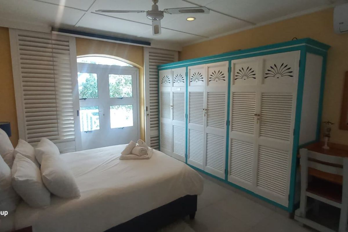A bedroom featuring built-in louvered wardrobes, a ceiling fan, split-system air conditioning, and access to a balcony through shuttered french doors.