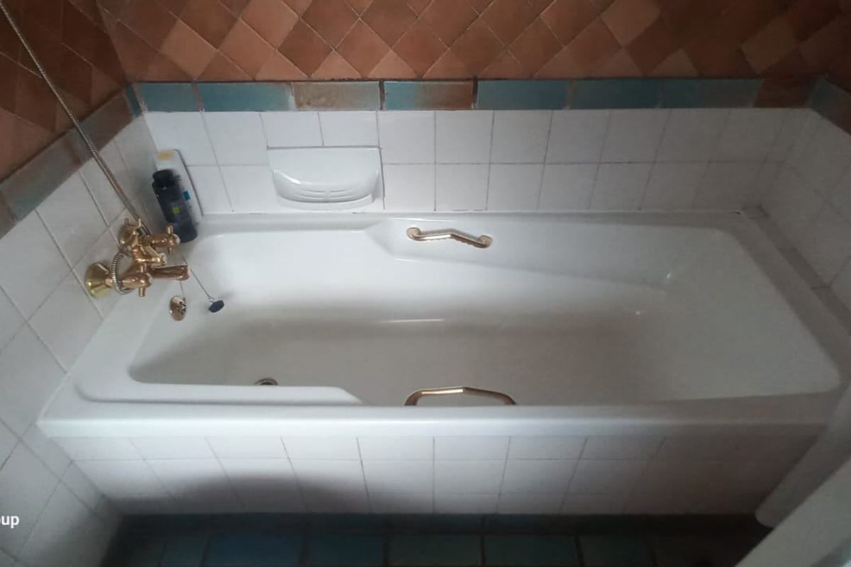 A bathroom featuring a built-in bathtub with gold-tone fixtures and decorative ceramic wall tiling.