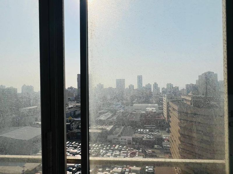 An elevated city view captured through a heavily soiled sliding glass door and balcony frame.