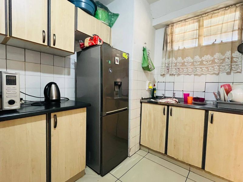 A compact kitchen featuring laminate cabinetry, tiled backsplash, and tiled flooring, offering a functional layout with potential for cosmetic updates.