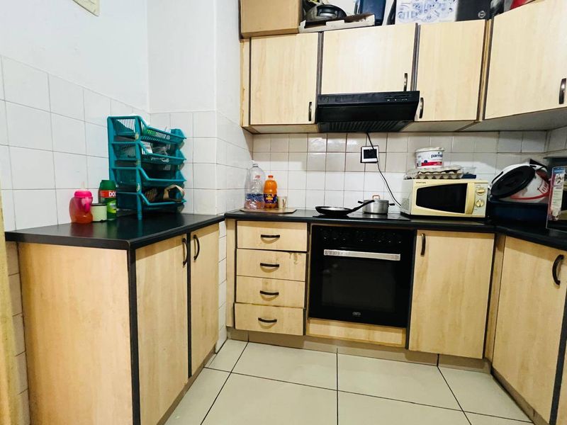 A functional kitchen featuring light wood-finish cabinetry, black countertops, a built-in oven, and an extractor fan, finished with tiled walls and flooring.
