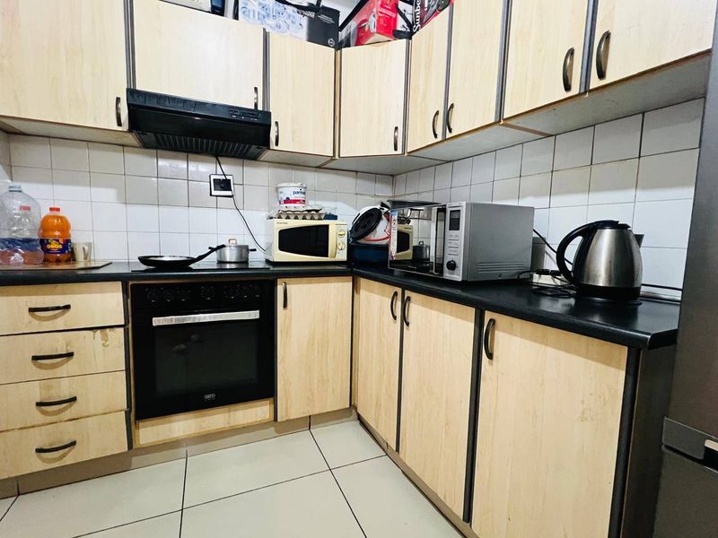 A functional kitchen featuring light wood-tone laminate cabinetry, black countertops, built-in oven, extractor fan, and tiled splashbacks.