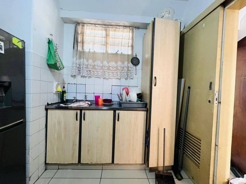 Compact kitchen area featuring built-in cabinetry, a stainless steel sink, and tiled splashback, offering a functional space in need of cosmetic updates.