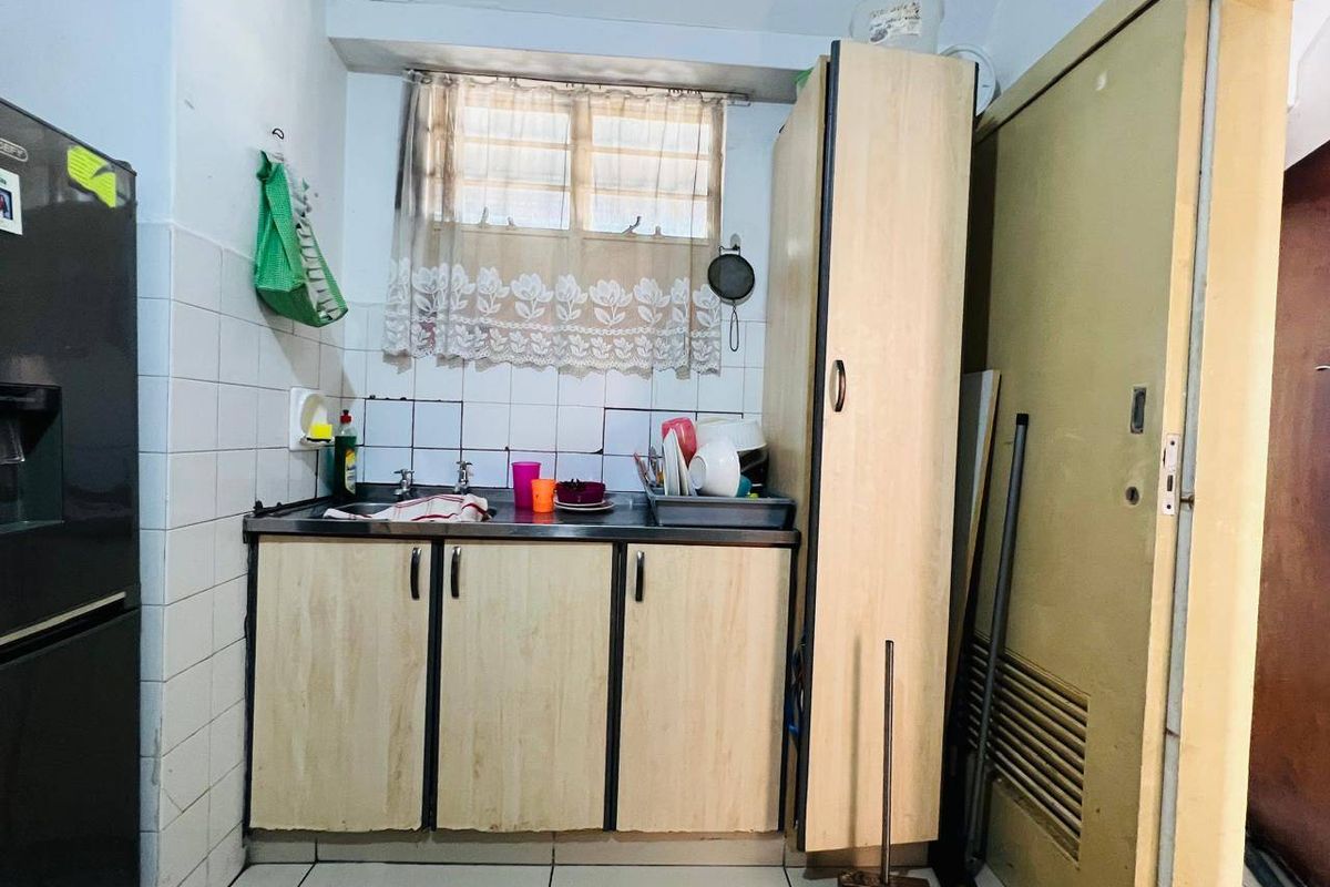 Compact kitchen area featuring built-in cabinetry, a stainless steel sink, and tiled splashback, offering a functional space in need of cosmetic updates.