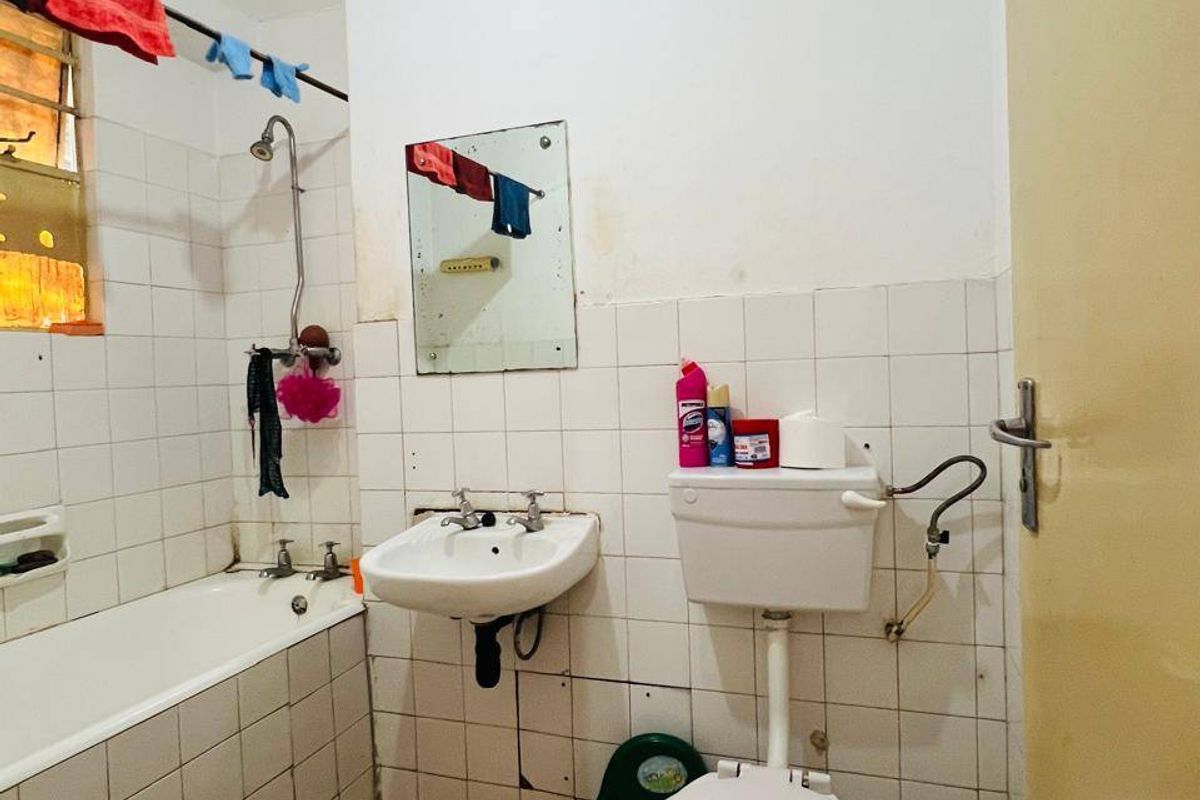 A functional bathroom featuring a bathtub, wall-mounted basin, and toilet with tiled finishes, currently requiring maintenance and cosmetic updates.